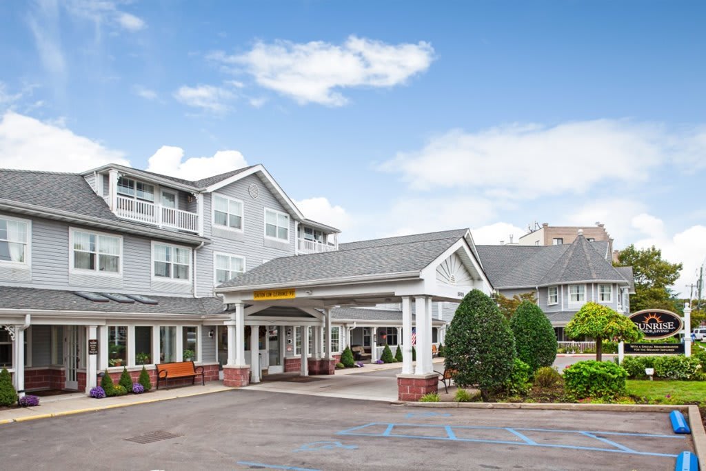 A hotel entrance with a neatly landscaped driveway under a blue sky with scattered clouds.