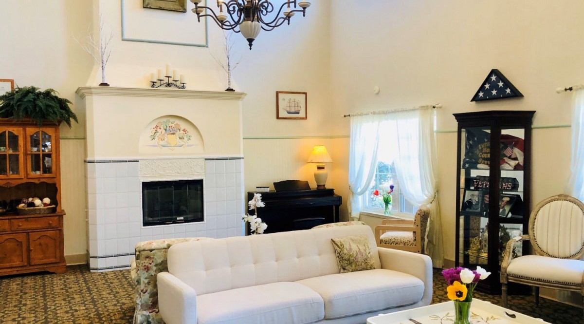A cozy living room featuring a white sofa, elegant chandelier, and a classical fireplace.