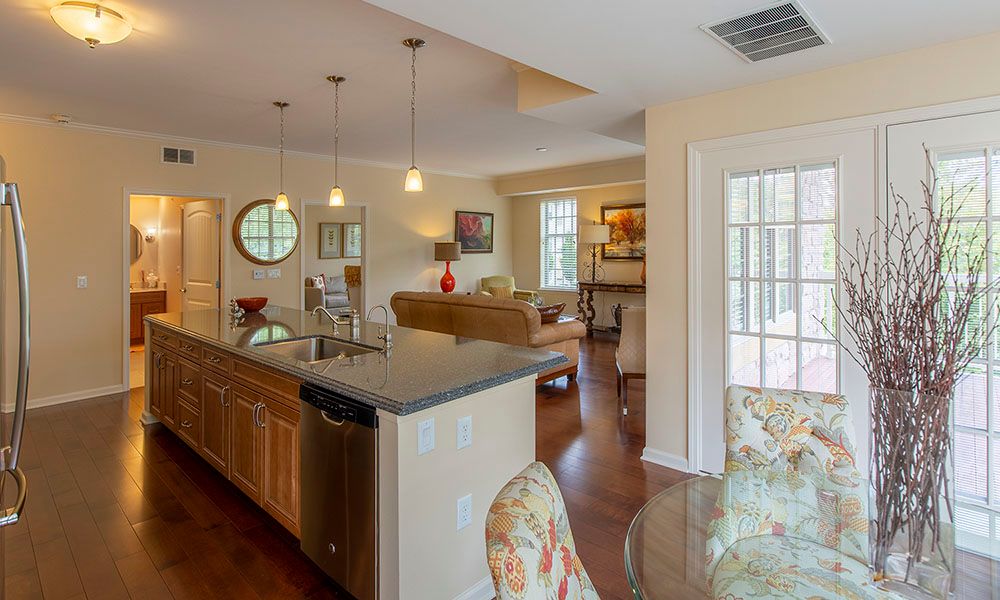 A modern open-concept living and kitchen area featuring wood flooring, pendant lighting, and a granite countertop.