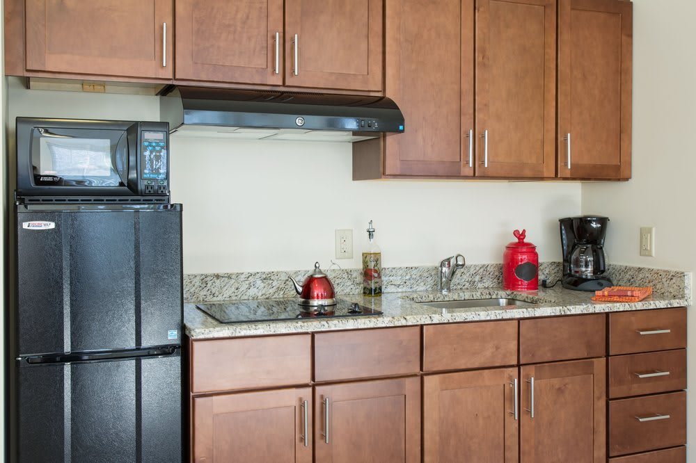 A modern kitchen with wooden cabinets, granite countertops, and various appliances including a refrigerator, stove, and coffee maker.
