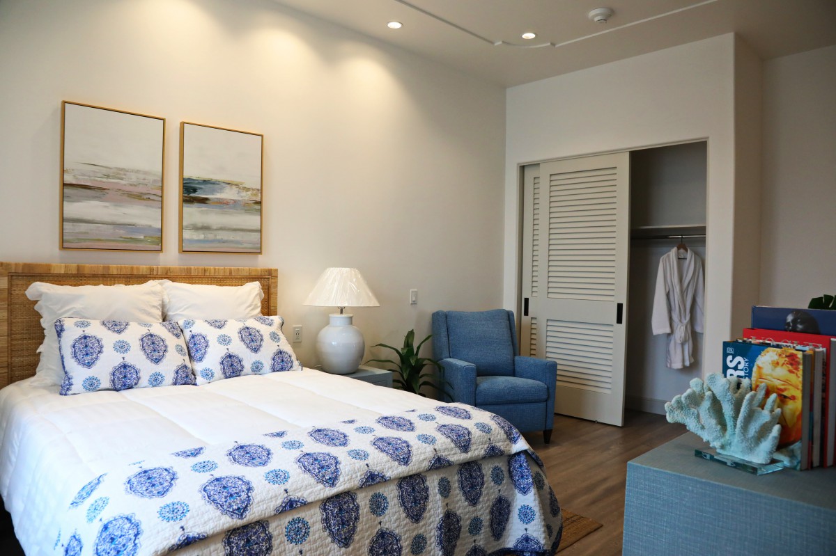 A cozy bedroom with a blue and white theme, featuring a comfortable bed, armchair, and closet.