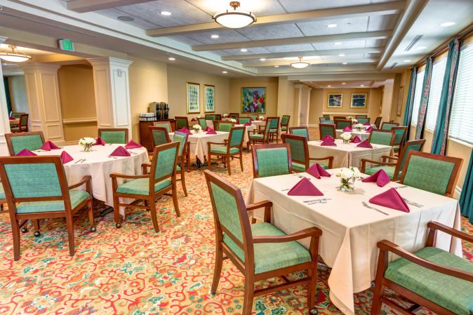 An elegantly arranged dining room with neatly set tables and chairs, featuring floral decorations and colorful napkins.
