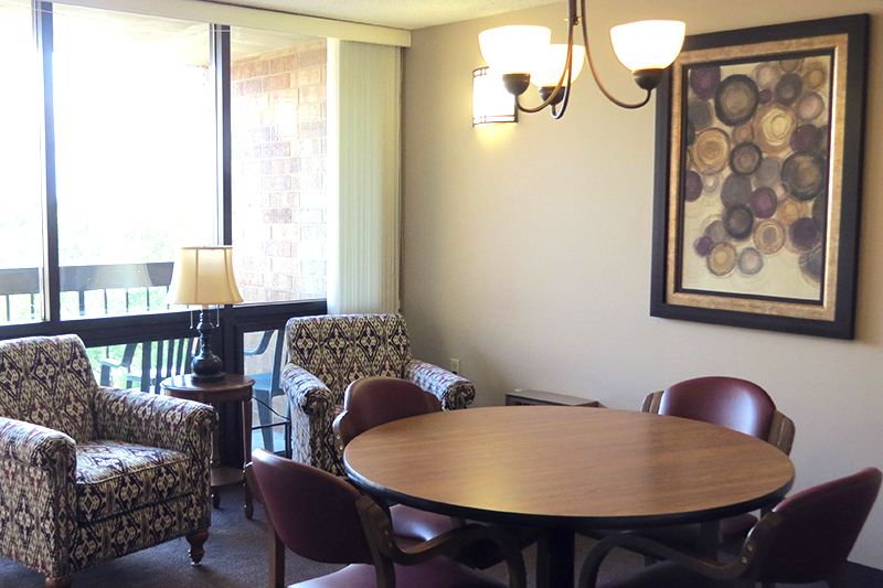 A cozy dining area with a round table and chairs, featuring a chandelier and artwork on the wall.