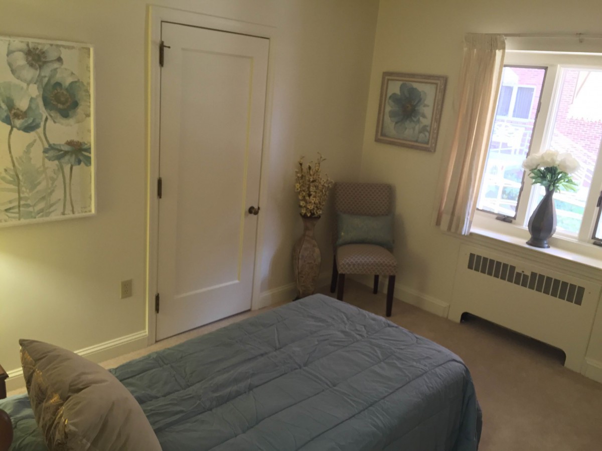 A neatly arranged bedroom with a bed, chair, and window.