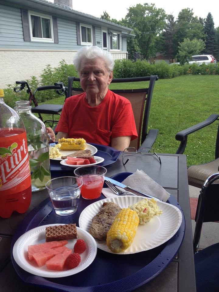 A person enjoying an outdoor meal with corn, watermelon, and soda on a sunny day.