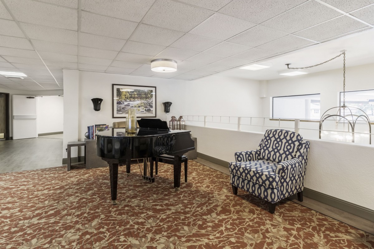A spacious room featuring a grand piano and a patterned chair, complemented by wall art and lighting.