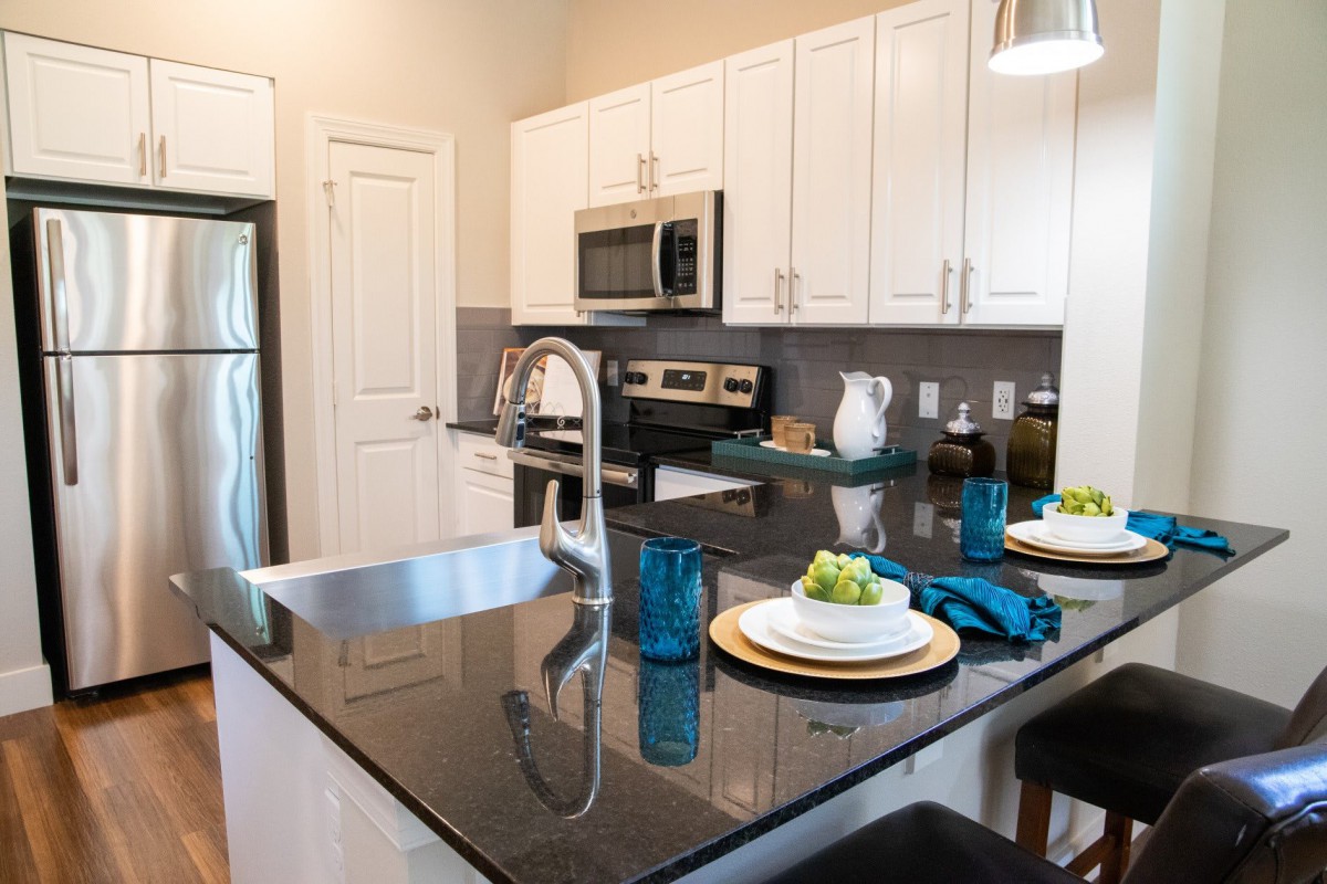 A modern kitchen with granite countertops and stainless steel appliances, featuring a cozy dining area with bar stools.