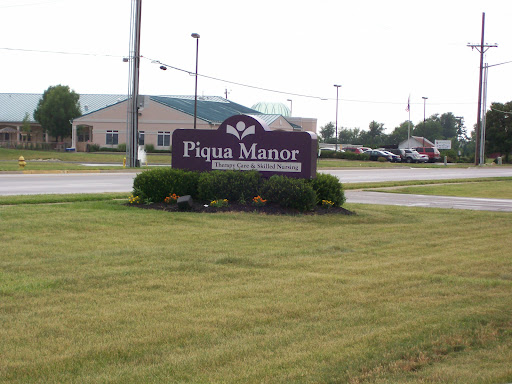 Piqua Manor sign in a grassy area with a building in the background.