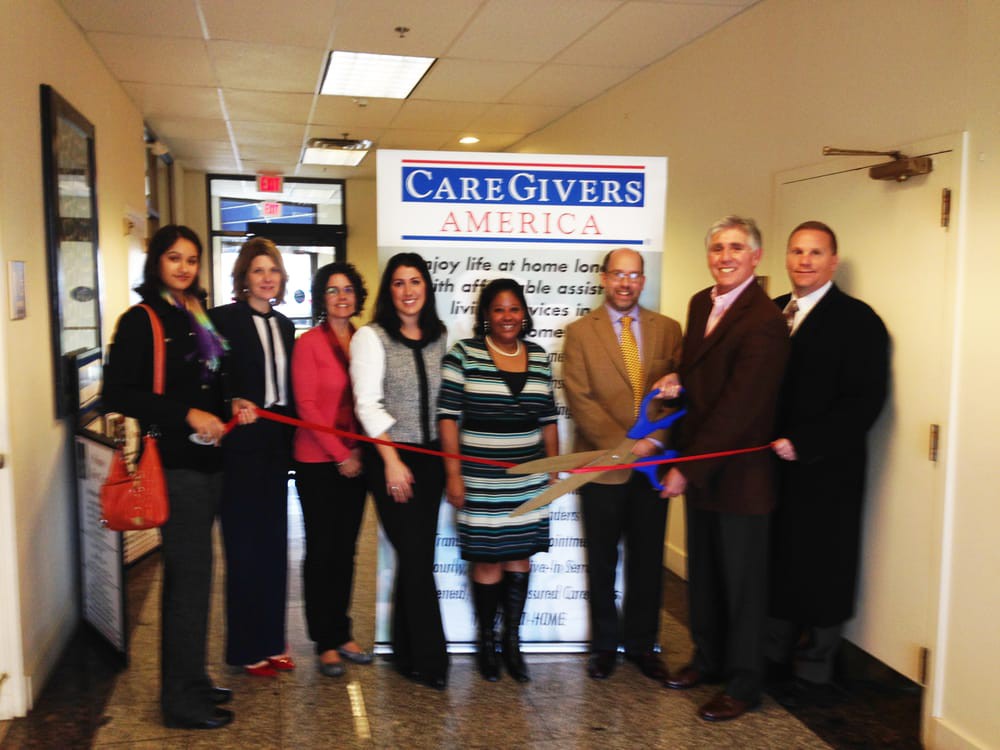 A group of people participate in a ribbon-cutting ceremony for the opening of CareGivers America.