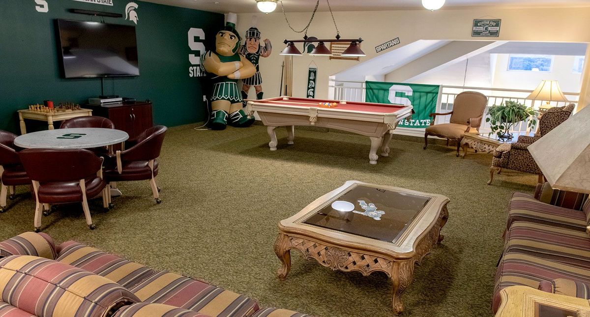 A sports-themed game room featuring a pool table, mascot figure, and team banners.