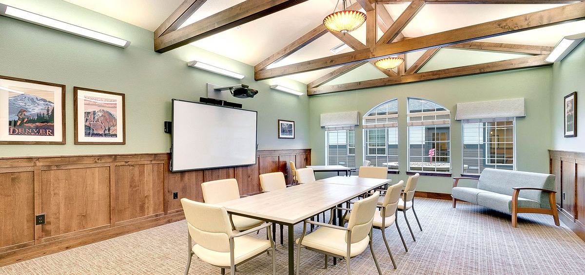 A well-lit conference room featuring a large table, several chairs, a projector, and a whiteboard.