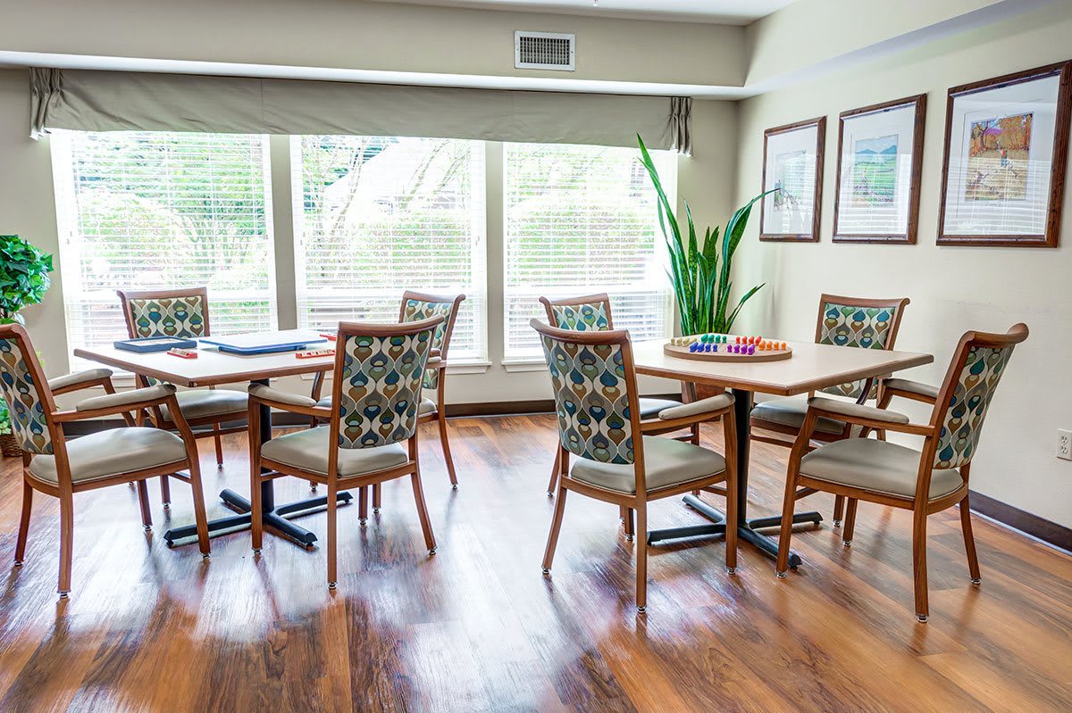A bright dining area with wooden floors, tables, chairs, and a large window.