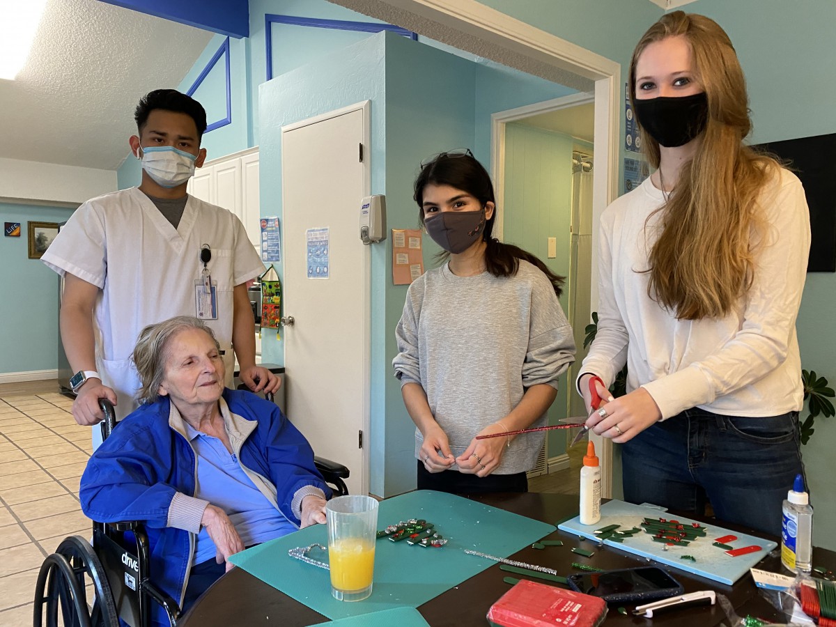 A group of people, including healthcare workers and students, caring for an elderly person in a wheelchair.