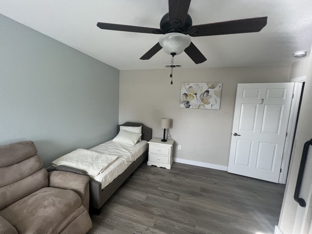 A minimalist bedroom featuring a single bed with white bedding, a ceiling fan, and modern decor.