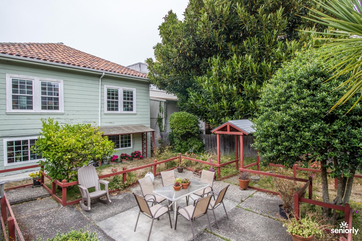 A cozy backyard patio area with a table and chairs, surrounded by lush greenery.