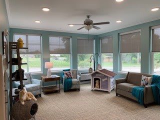 A cozy living room with ample natural light, featuring comfortable seating and a pet house.