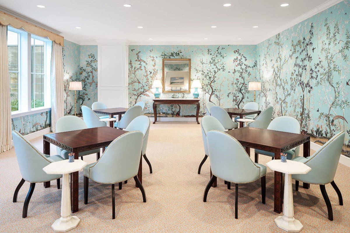 An elegant dining room with pastel-colored chairs and tables, featuring floral wallpaper and soft lighting.