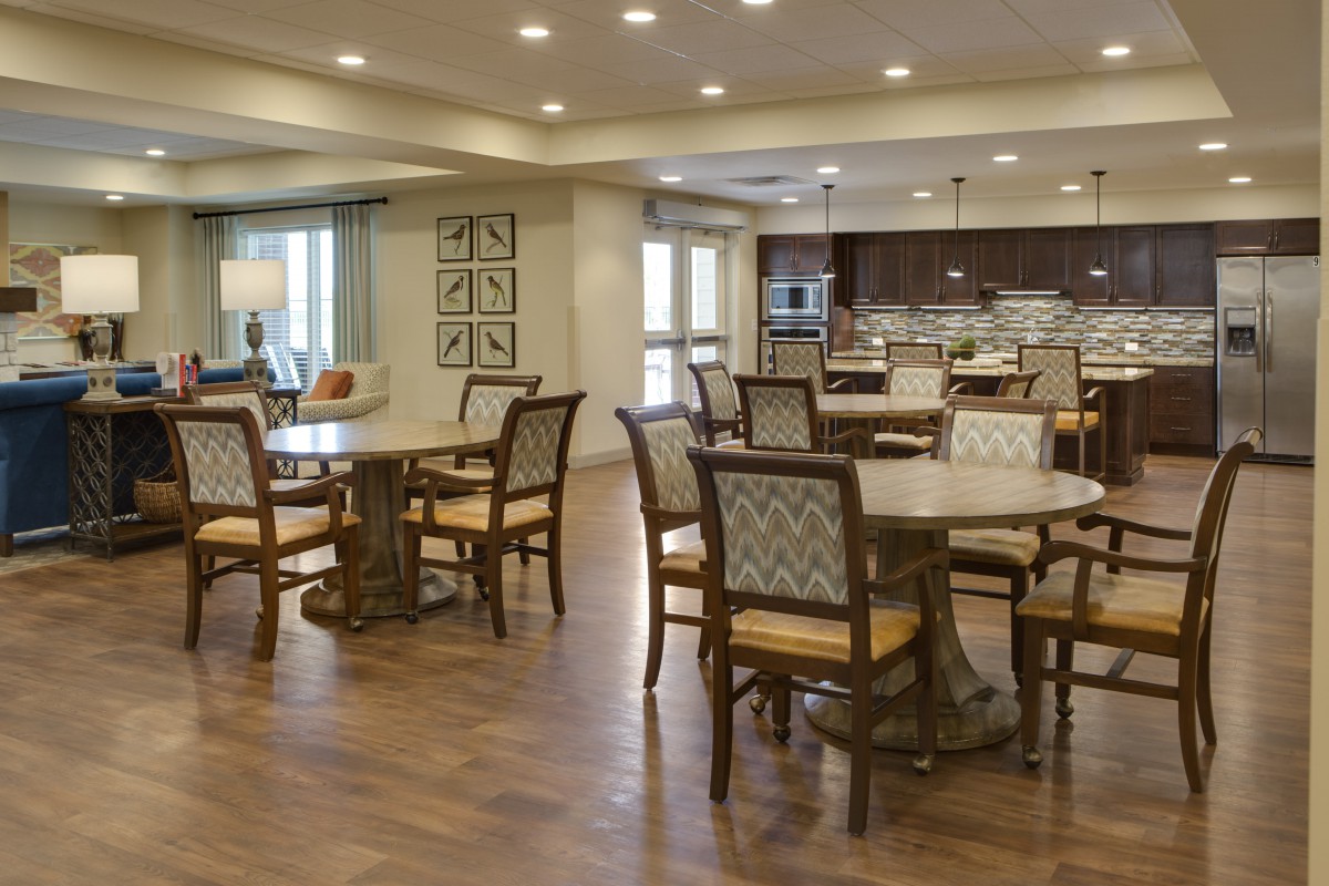 A spacious and elegantly designed dining area with multiple tables and chairs, featuring warm lighting and a wooden floor.