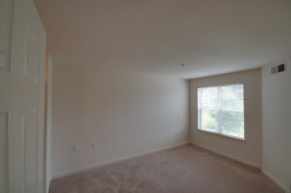 An empty room with carpet flooring and a large window letting in natural light.