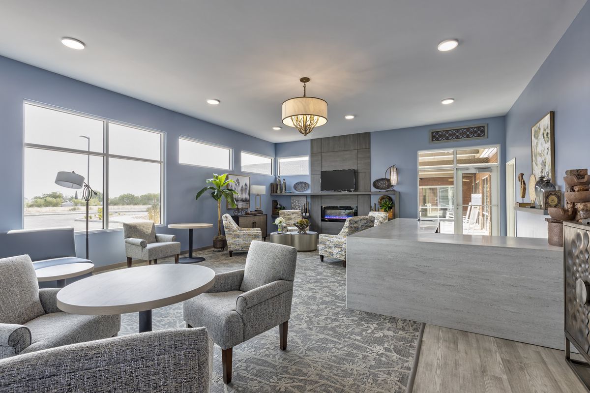 A modern living room with ample seating, featuring a chandelier and large windows.