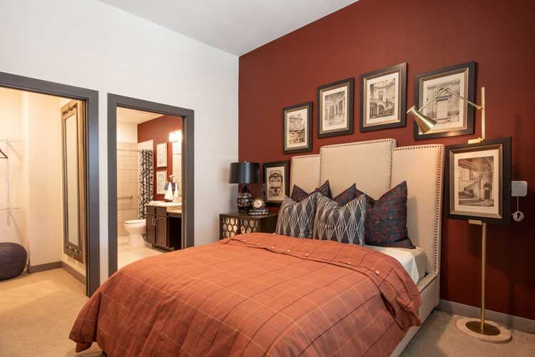 A stylish bedroom with a warm red accent wall, a comfortable bed adorned with patterned pillows, and framed artwork above the headboard.