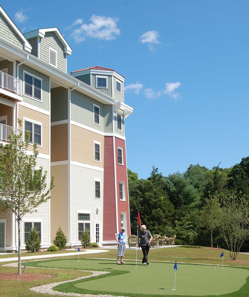 A couple of people standing on the lawn near a multi-story apartment building with trees in the background.