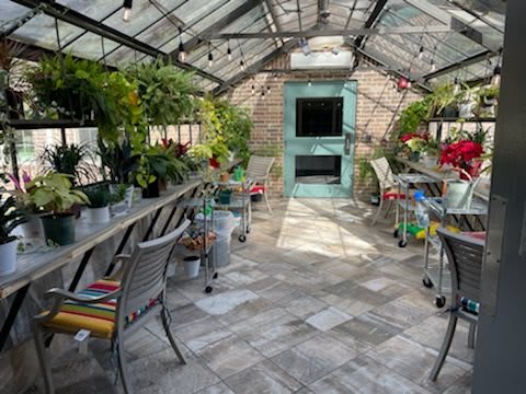 A beautifully arranged greenhouse filled with various plants and flowers, with seating available for relaxation among nature.