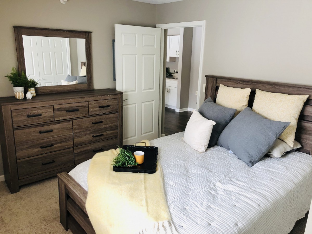 A cozy bedroom featuring a neatly made bed with decorative pillows and a wooden dresser with a mirror.