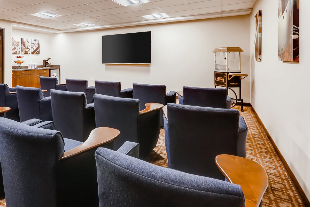 A small movie theater or conference room with rows of comfortable chairs facing a large screen.