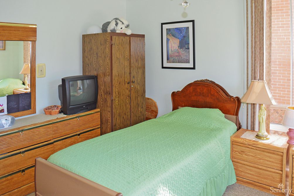A small bedroom with a single bed, wooden furniture, and an old-style television.