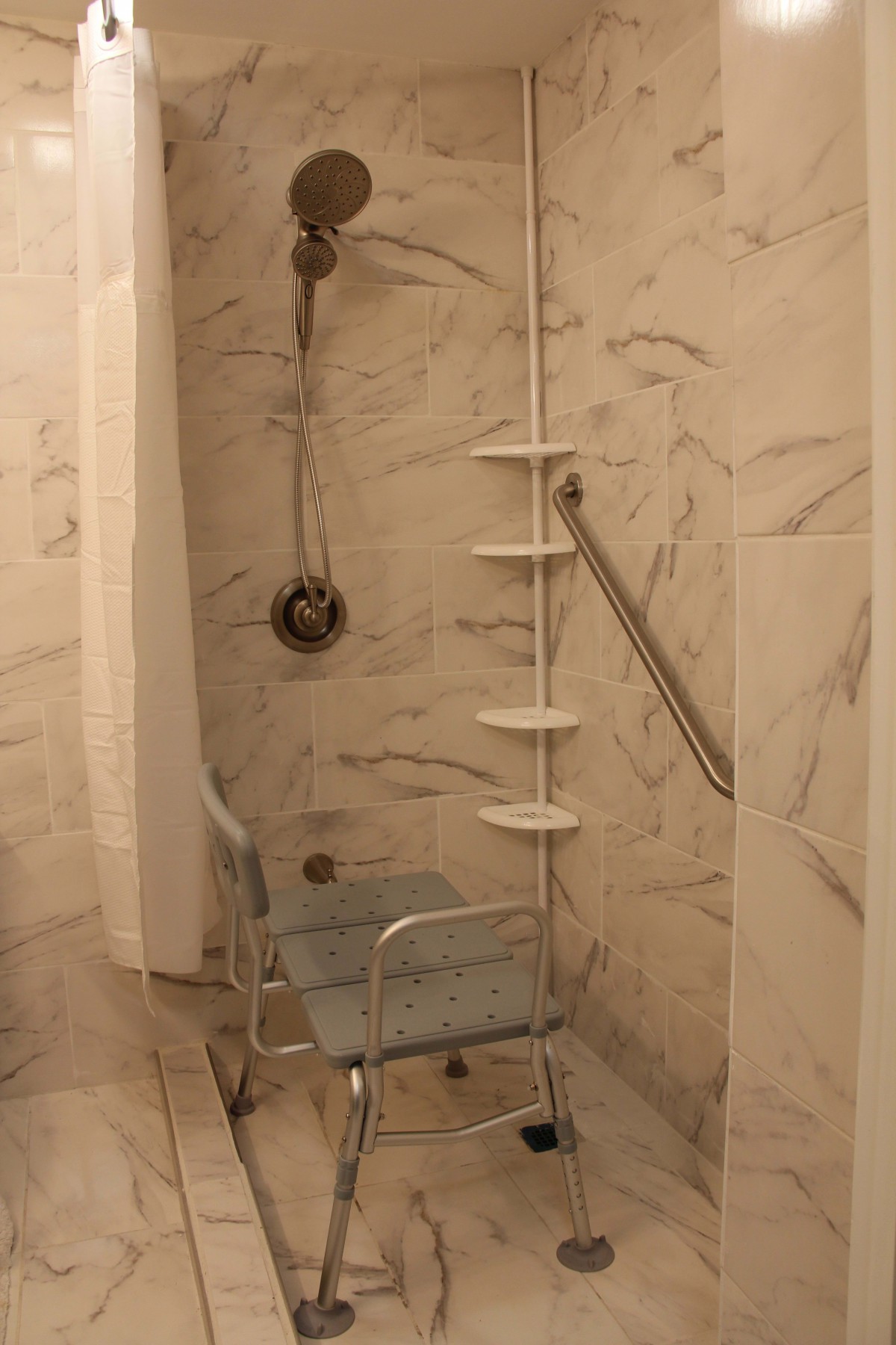 A marble-tiled bathroom featuring a wheelchair accessible shower with a shower chair and grab bar.