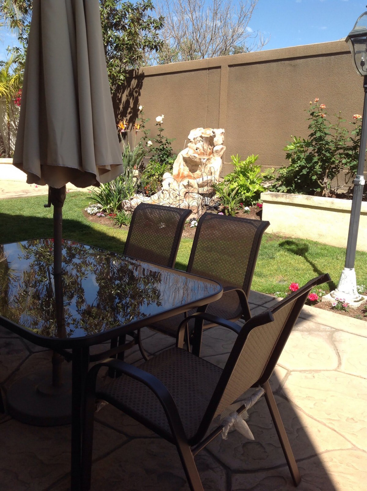 A sunny patio with a glass table, chairs, and garden view.