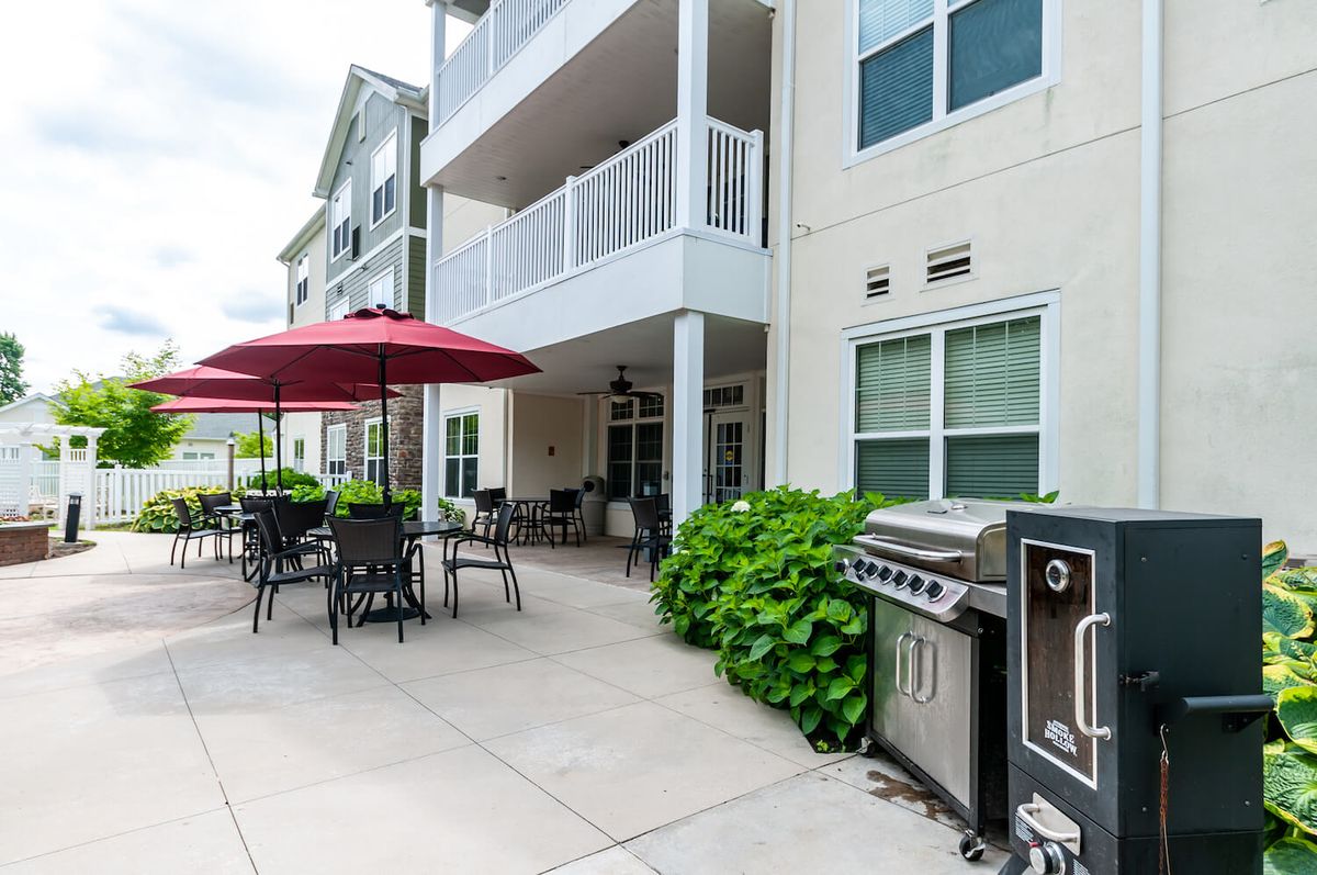 An outdoor patio area of an apartment complex featuring seating with umbrellas and a grill.