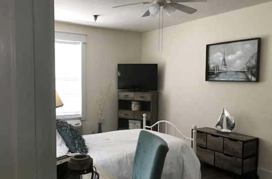 A cozy bedroom with a bed, television, and ceiling fan.
