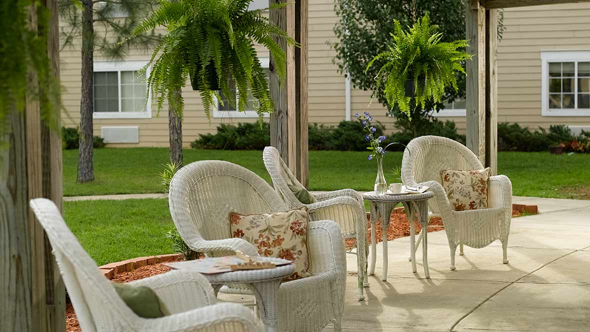 A cozy patio setup with wicker chairs and tables, surrounded by lush greenery.