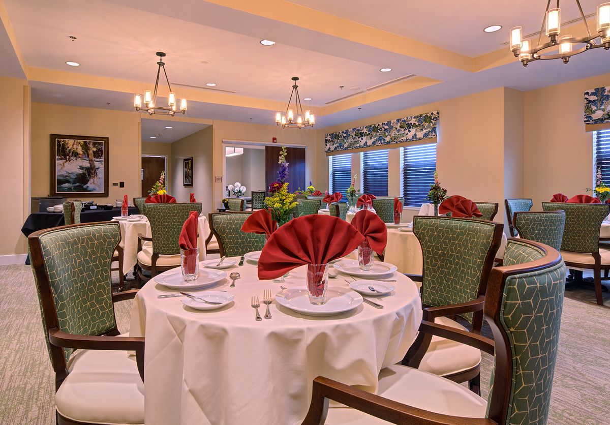 An elegantly set dining room with neatly arranged tables, chairs, and decorative chandeliers.