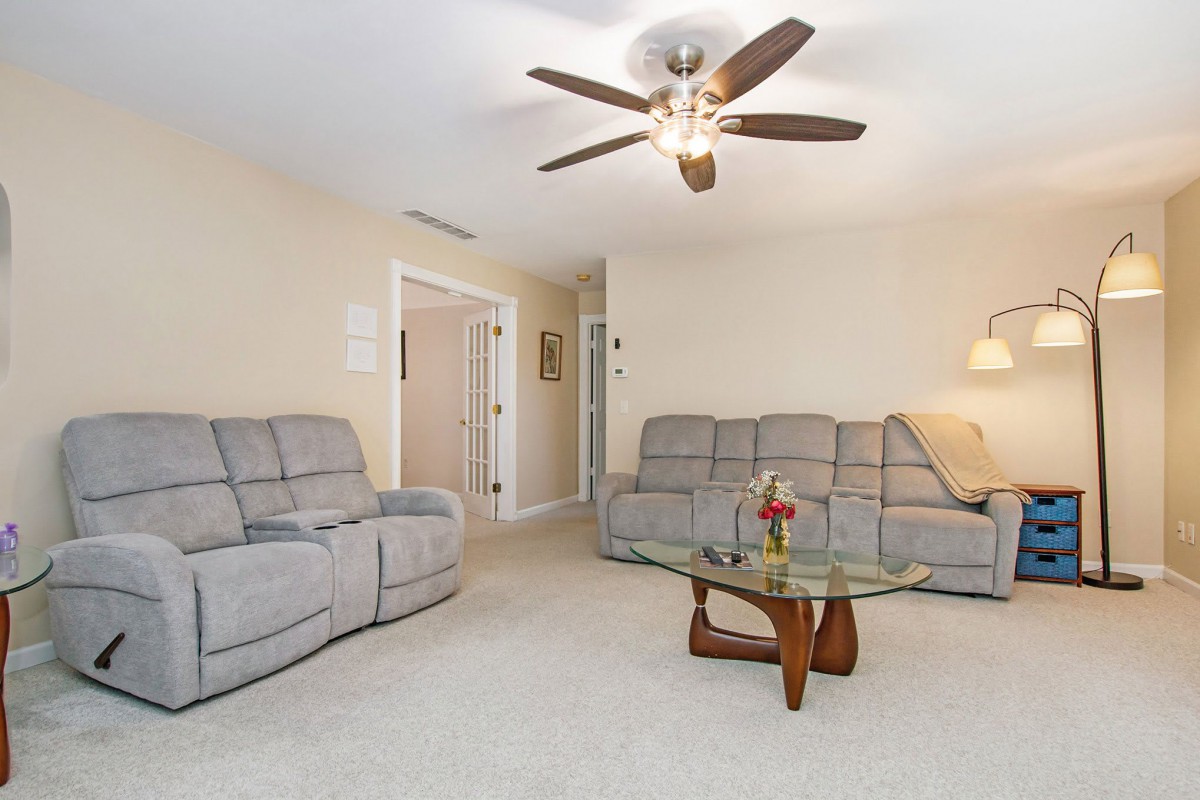 A cozy living room featuring two gray sofas, a ceiling fan, and a stylish glass coffee table.