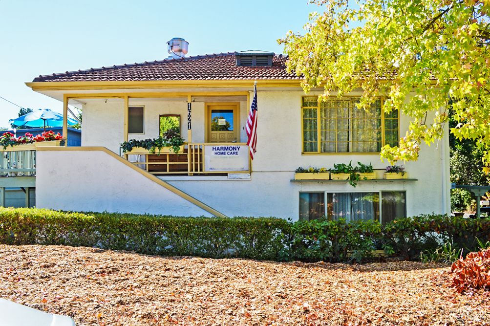 A residential house with a flag displayed outside, surrounded by trees and bushes on a sunny day.