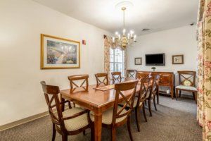 A formal dining room with a large wooden table, surrounded by chairs, featuring a chandelier and artwork on the walls.