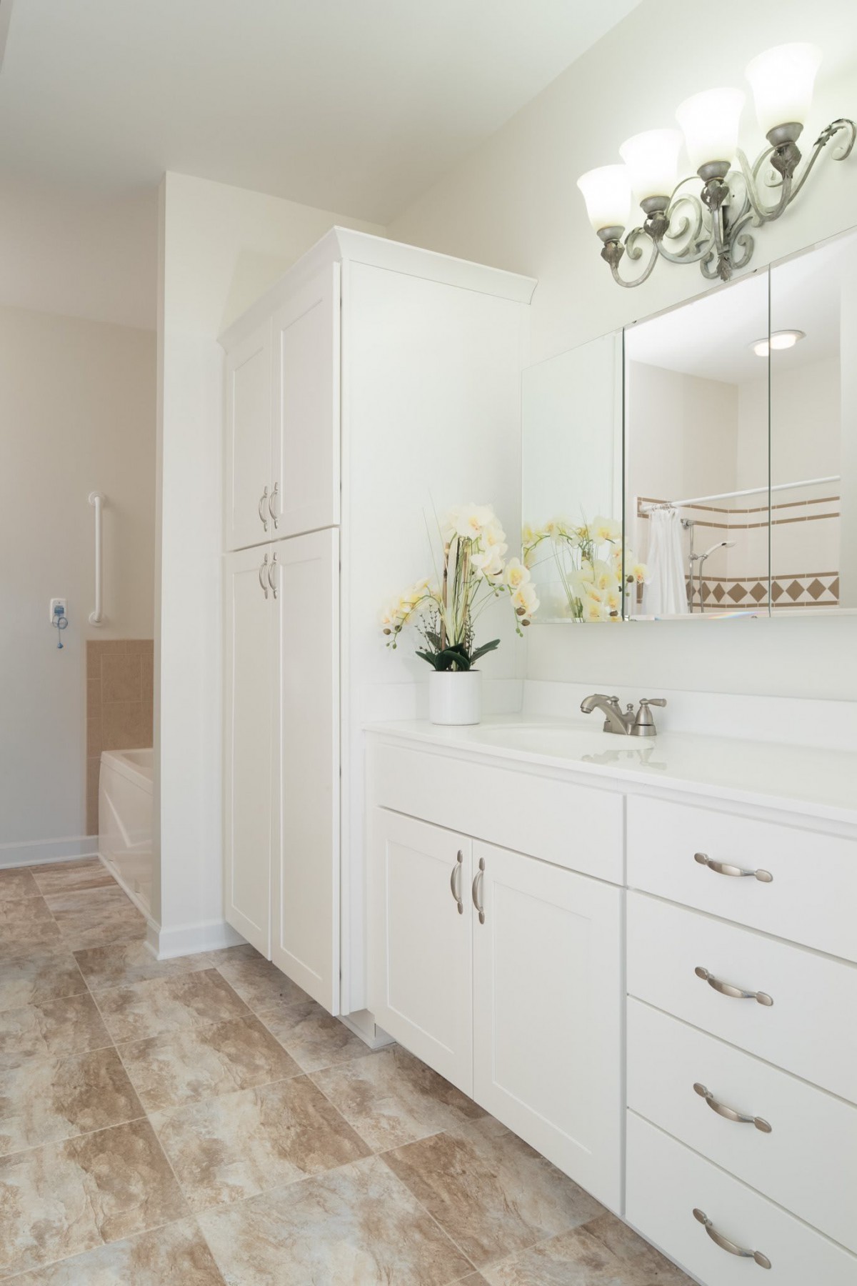 A modern bathroom with white cabinets, a large mirror, and an orchid decoration.