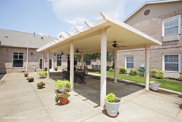 A spacious outdoor patio area with a pergola, featuring tables and chairs, surrounded by potted plants.