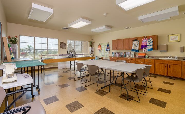 An art classroom with tables and chairs, featuring large windows and cabinets.