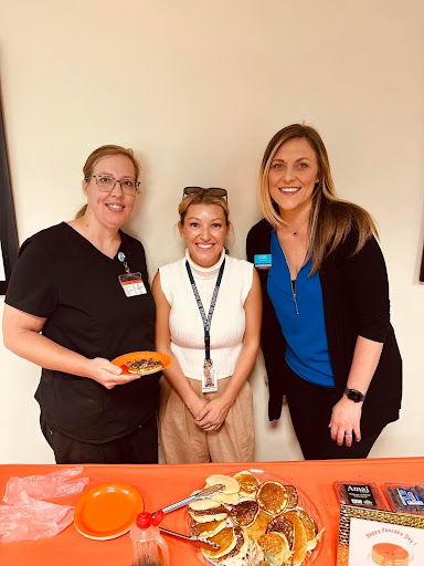 A group of three women posing together at a workplace event.