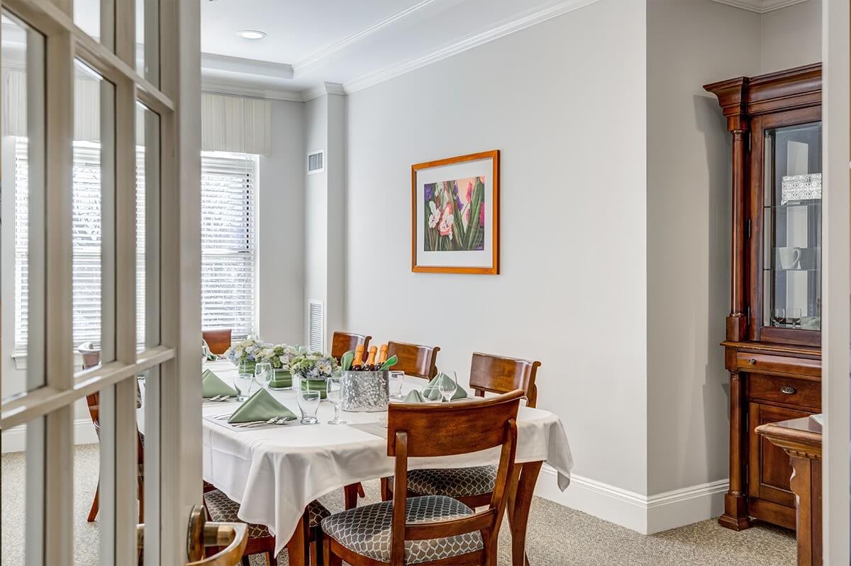 A well-lit dining room with a table set for a meal, featuring wooden chairs and a framed artwork on the wall.