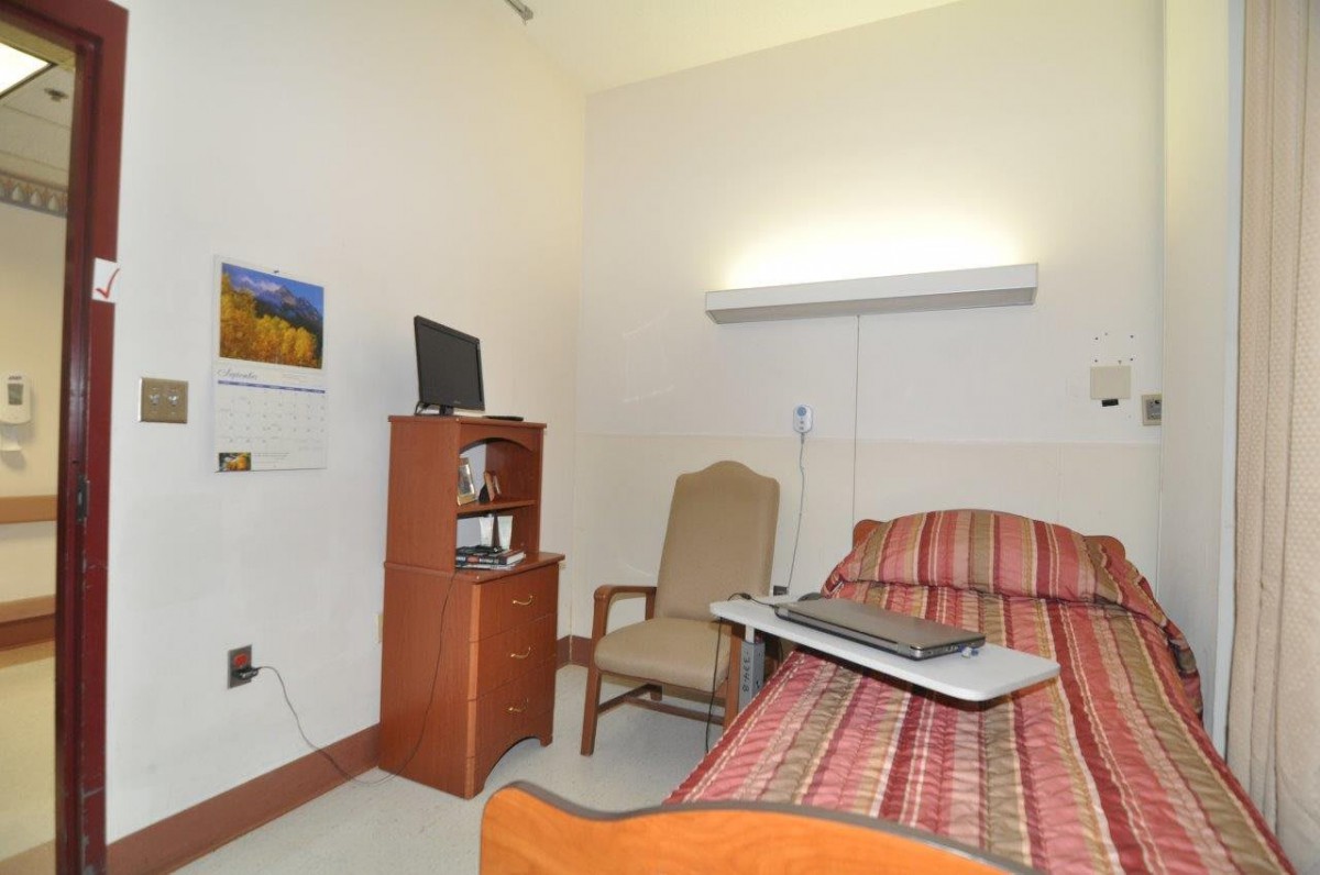 A hospital room with a bed, chair, and television setup.