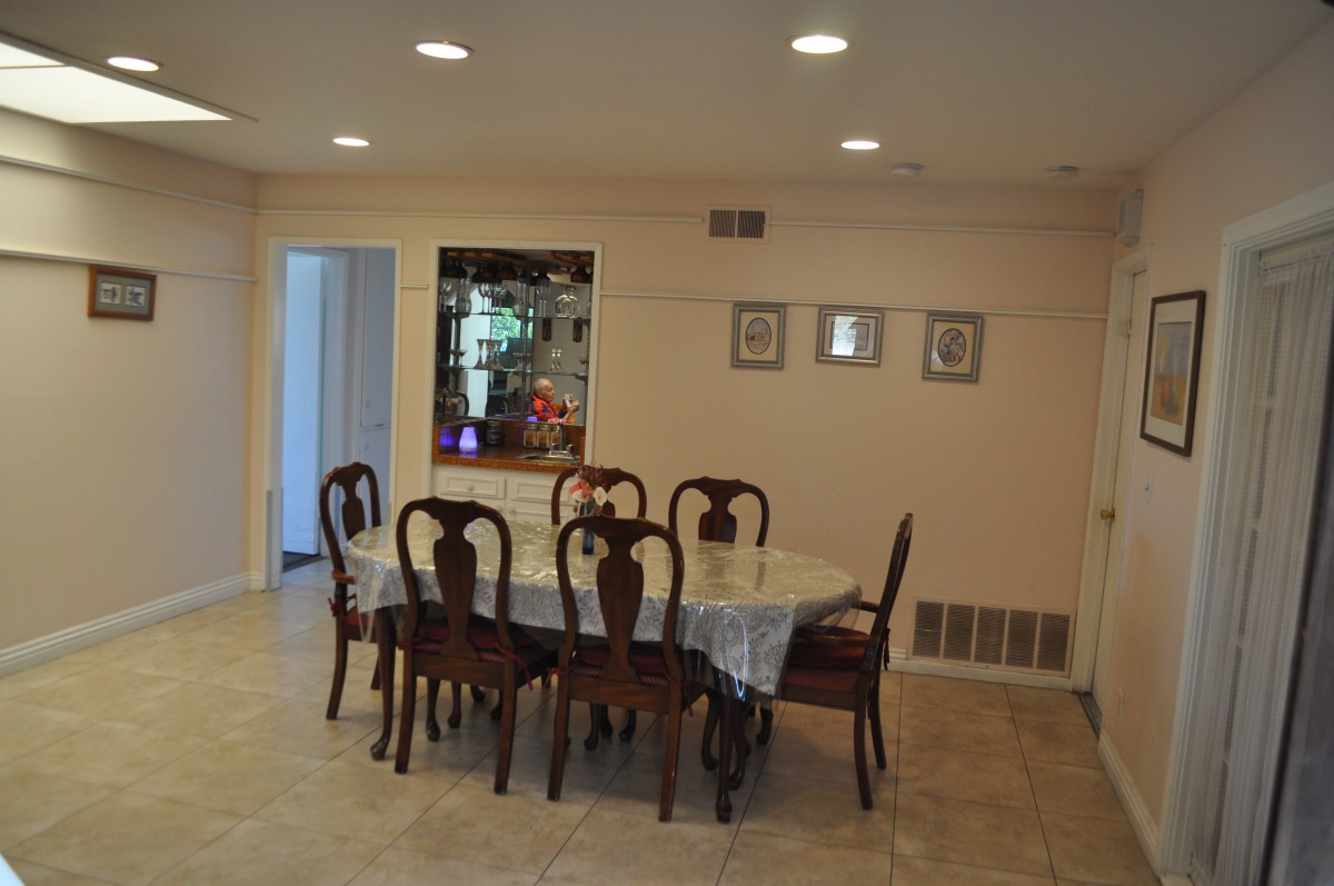 A well-lit dining area featuring a large table and chairs with a decorative mirror on the wall.