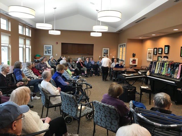 A community gathering of elderly people attending an indoor event featuring a piano performance.
