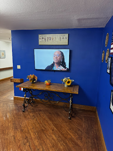 A cozy living room corner featuring a blue wall, a wooden table with decorative items, and a television displaying content.