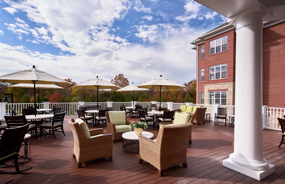 An inviting outdoor patio area with wicker chairs and tables under large umbrellas, set against a backdrop of a brick building and a partly cloudy sky.