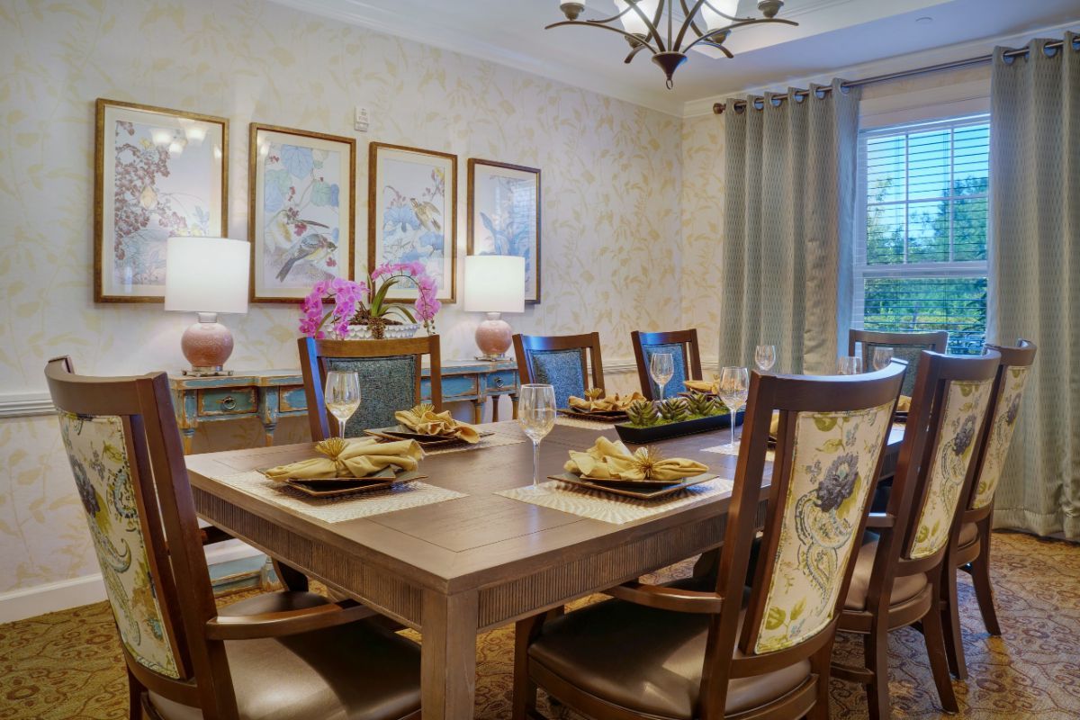 A well-decorated dining room with a large table set for a meal, surrounded by elegant chairs and adorned with artwork and soft lighting.